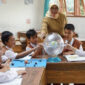 Terlihat ibu guru sedang fokus mengajar muridnya di  ruang kelas.